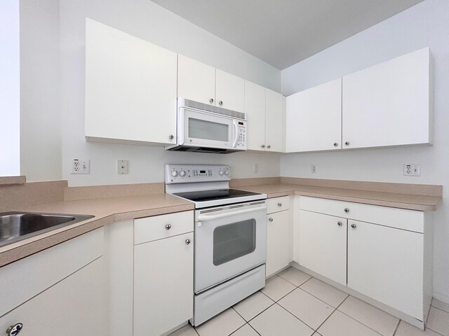 kitchen with light tile patterned flooring, a breakfast bar area, white cabinetry, white appliances, and kitchen peninsula