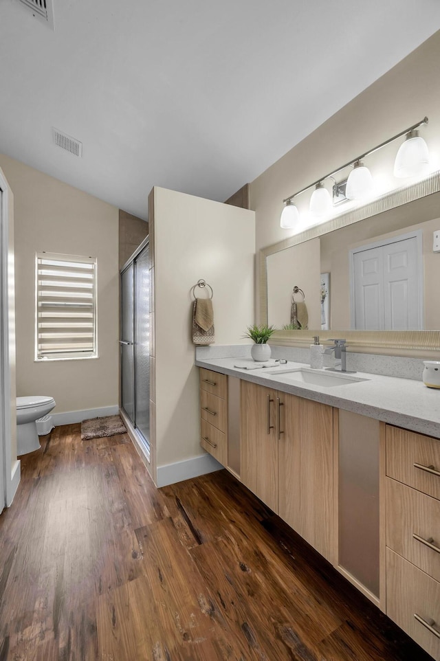 bathroom featuring hardwood / wood-style flooring, vanity, toilet, and a shower with shower door