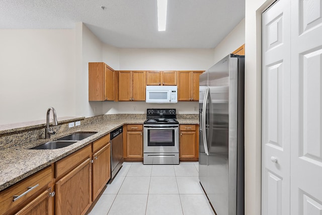 kitchen with appliances with stainless steel finishes, sink, light stone counters, light tile patterned floors, and a textured ceiling