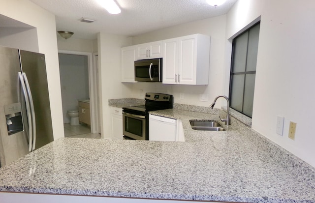 kitchen featuring appliances with stainless steel finishes, white cabinetry, light stone countertops, and sink