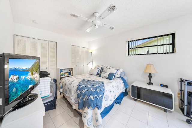 tiled bedroom with a textured ceiling, two closets, and ceiling fan