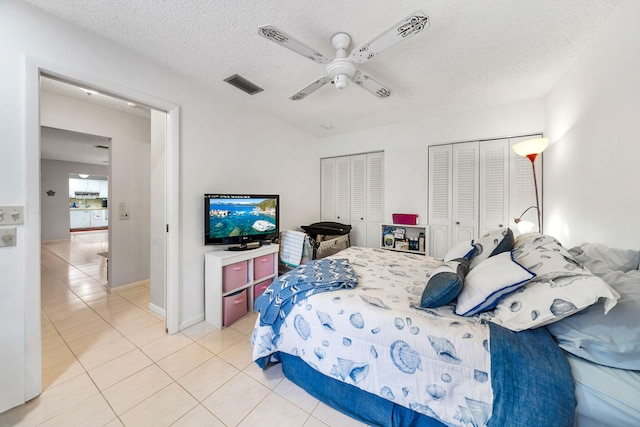 bedroom with ceiling fan, multiple closets, a textured ceiling, and light tile patterned floors