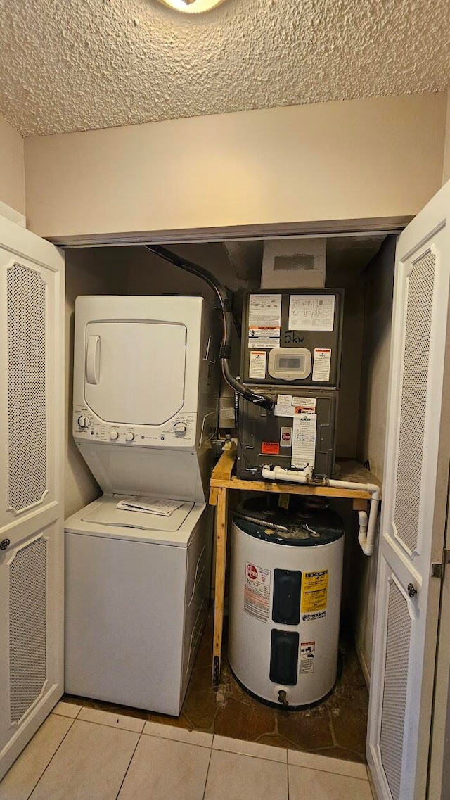 clothes washing area with water heater, stacked washer / dryer, a textured ceiling, and light tile patterned floors