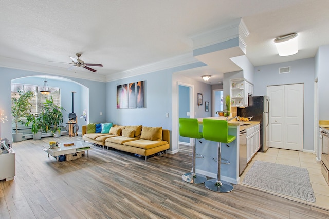 interior space with light wood-type flooring, a textured ceiling, ceiling fan, and ornamental molding