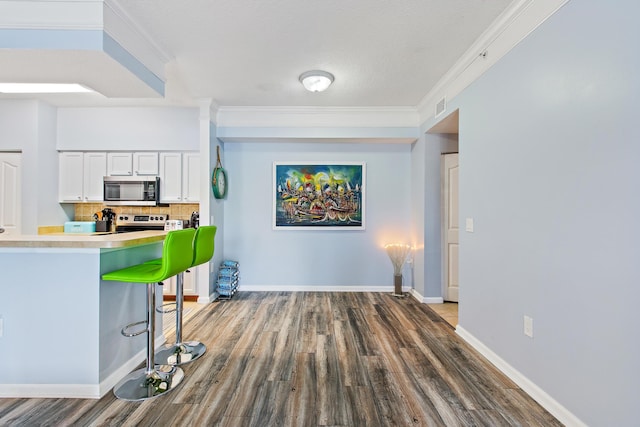 kitchen featuring white cabinetry, stainless steel appliances, tasteful backsplash, a kitchen breakfast bar, and ornamental molding