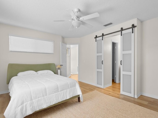 bedroom featuring a textured ceiling, a barn door, wood-type flooring, and ceiling fan