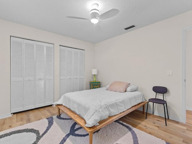 bedroom with hardwood / wood-style floors, multiple closets, a textured ceiling, and ceiling fan