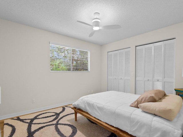 bedroom featuring hardwood / wood-style flooring, two closets, a textured ceiling, and ceiling fan