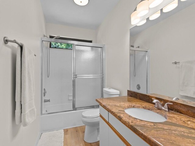 full bathroom with vanity, toilet, enclosed tub / shower combo, and hardwood / wood-style floors