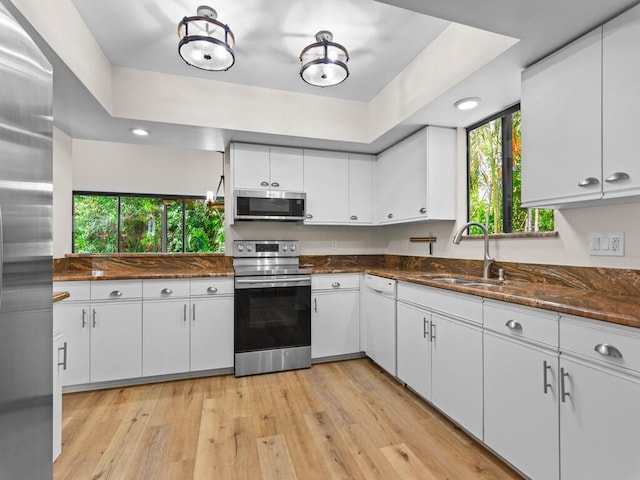 kitchen featuring dark stone countertops, sink, light wood-type flooring, white cabinetry, and appliances with stainless steel finishes