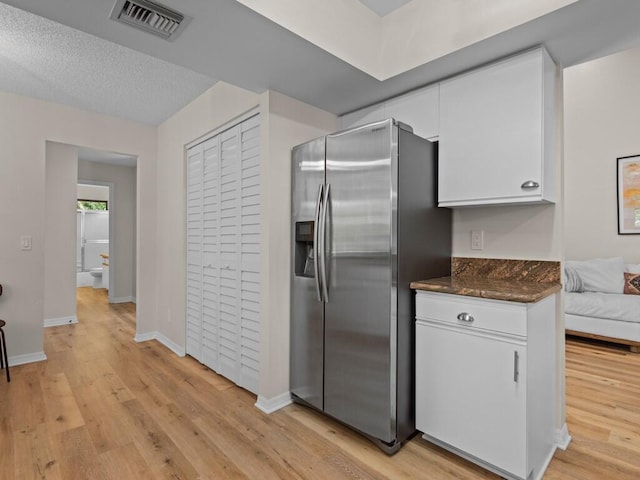 kitchen with white cabinets, stainless steel fridge with ice dispenser, a textured ceiling, light hardwood / wood-style flooring, and dark stone countertops