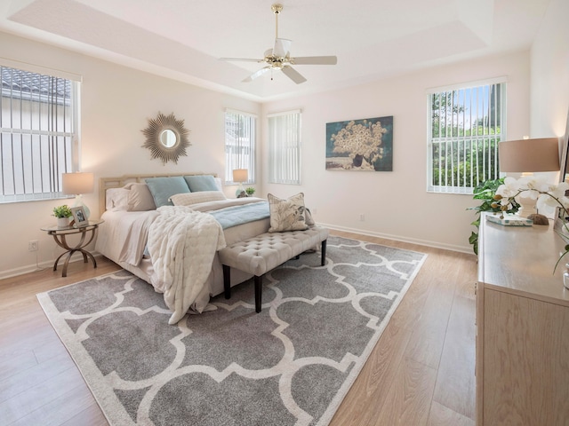 bedroom featuring light hardwood / wood-style flooring, a raised ceiling, and ceiling fan