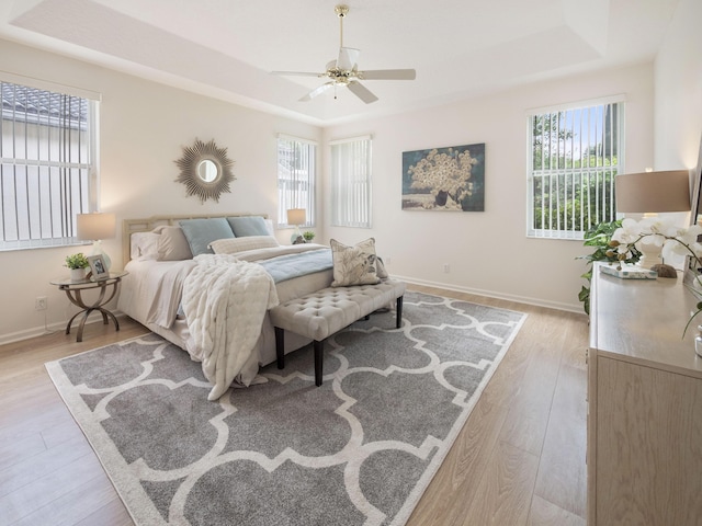 bedroom with light wood-style floors, baseboards, a tray ceiling, and ceiling fan