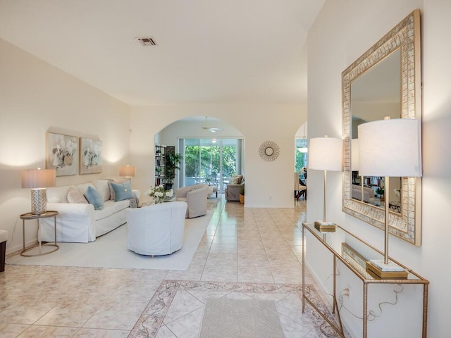 living room featuring arched walkways, light tile patterned floors, visible vents, and baseboards