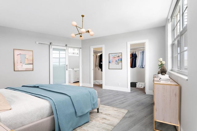 bedroom with a barn door, baseboards, wood finished floors, a walk in closet, and a closet