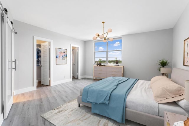 bedroom with a chandelier, a barn door, baseboards, and light wood-style floors