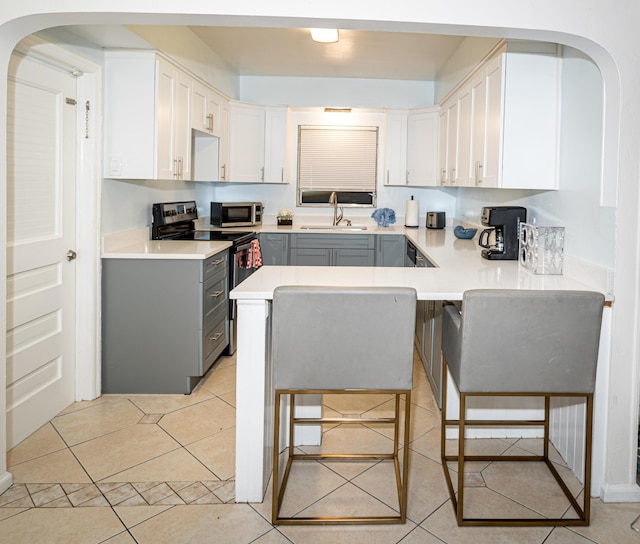 kitchen featuring gray cabinets, appliances with stainless steel finishes, a breakfast bar, sink, and white cabinets