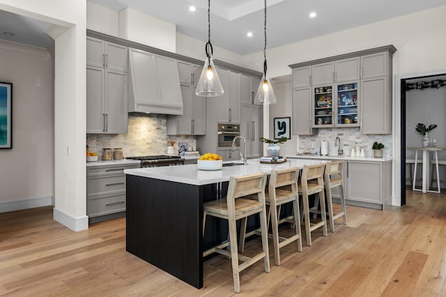 kitchen with oven, a center island with sink, light hardwood / wood-style flooring, backsplash, and gray cabinetry