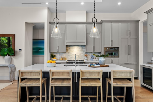 kitchen featuring a center island with sink, sink, paneled built in fridge, gray cabinets, and stainless steel oven