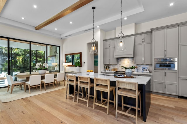 kitchen with oven, a kitchen island with sink, light wood-type flooring, and gray cabinets