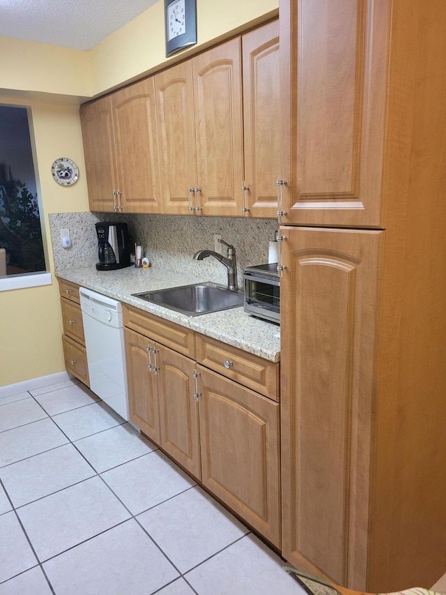 kitchen with backsplash, white dishwasher, sink, light stone countertops, and light tile patterned floors