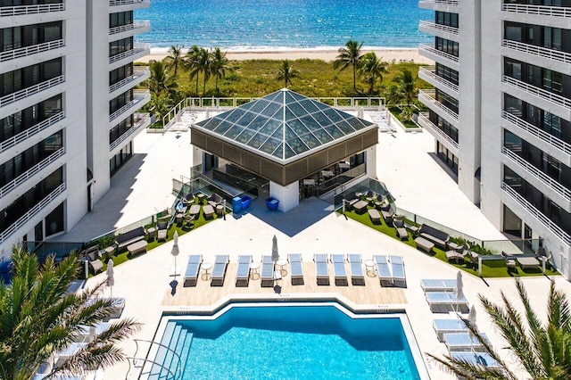 view of swimming pool with a water view, a patio area, and a beach view