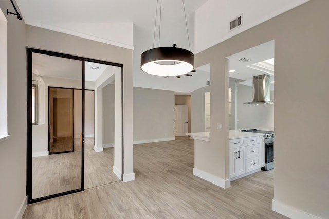 interior space featuring light hardwood / wood-style floors, wall chimney range hood, white cabinetry, and stainless steel range with electric stovetop