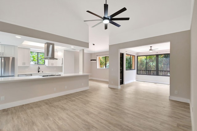 unfurnished living room featuring ceiling fan, a sink, light wood-style floors, plenty of natural light, and high vaulted ceiling