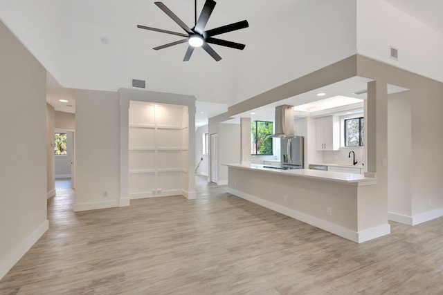 unfurnished living room featuring light wood-style floors, a sink, baseboards, recessed lighting, and a high ceiling