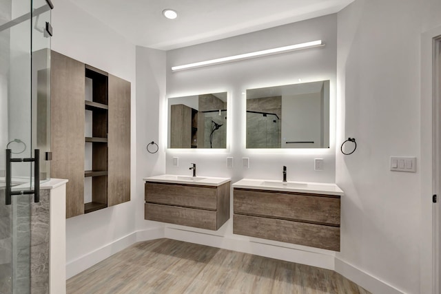 full bathroom with a stall shower, wood finished floors, two vanities, and baseboards