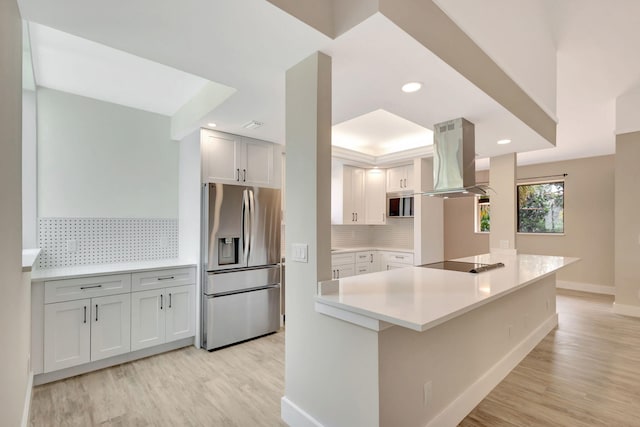 kitchen featuring stainless steel refrigerator with ice dispenser, black electric cooktop, island range hood, baseboards, and backsplash