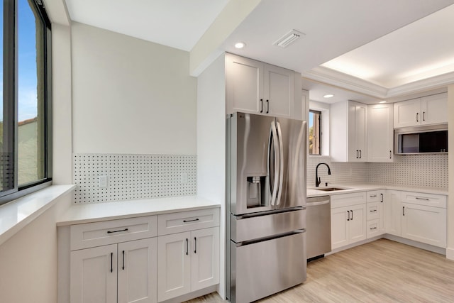 kitchen with tasteful backsplash, stainless steel appliances, sink, light hardwood / wood-style floors, and white cabinets