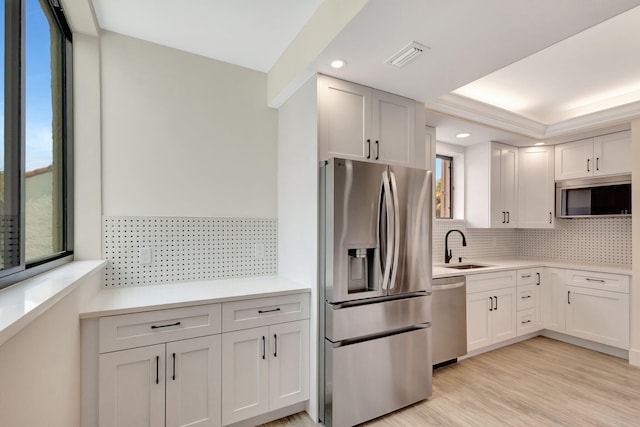 kitchen featuring stainless steel appliances, a sink, backsplash, light countertops, and light wood-style floors
