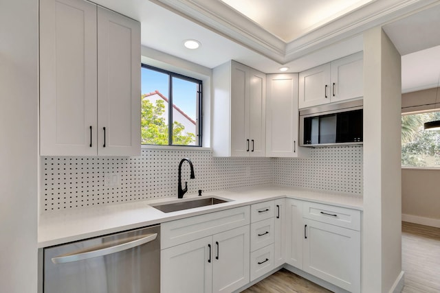 kitchen featuring appliances with stainless steel finishes, a sink, decorative backsplash, light countertops, and light wood-style flooring