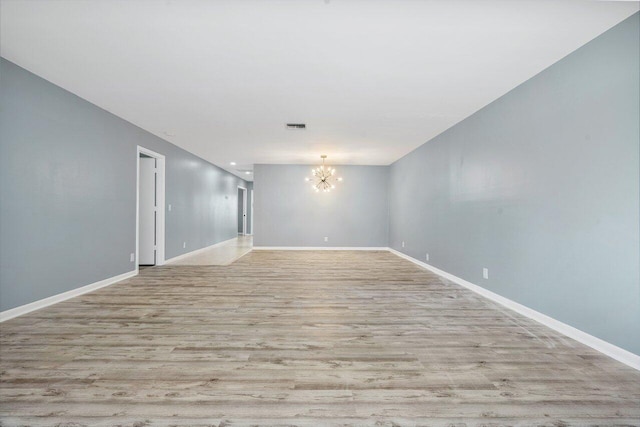 spare room with a notable chandelier and light hardwood / wood-style floors