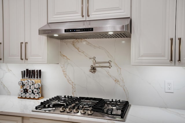 kitchen with white cabinetry, range hood, light stone counters, decorative backsplash, and stainless steel gas stovetop