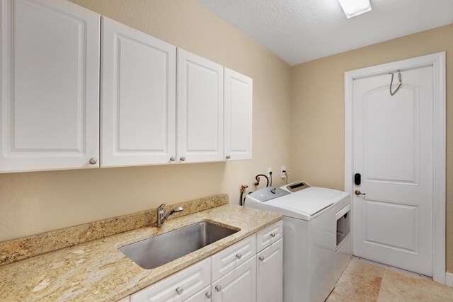 laundry area with sink, cabinets, a textured ceiling, light tile patterned floors, and washer and clothes dryer