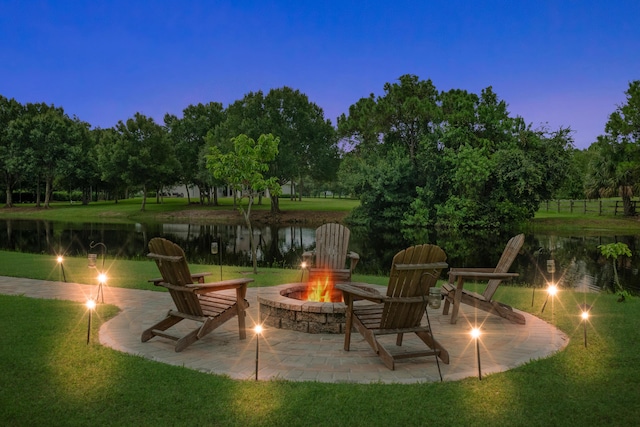 patio terrace at dusk with a fire pit, a lawn, and a water view