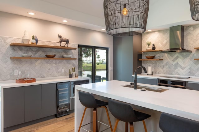 kitchen with tasteful backsplash, wine cooler, range hood, light hardwood / wood-style floors, and sink