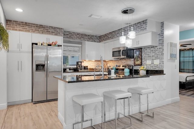 kitchen featuring white cabinetry, decorative light fixtures, dark stone counters, a kitchen breakfast bar, and stainless steel appliances