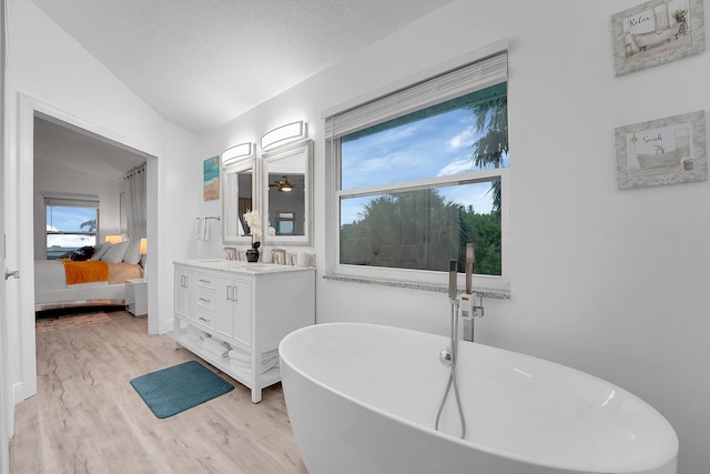 bathroom with hardwood / wood-style floors, a bathtub, vanity, a textured ceiling, and vaulted ceiling