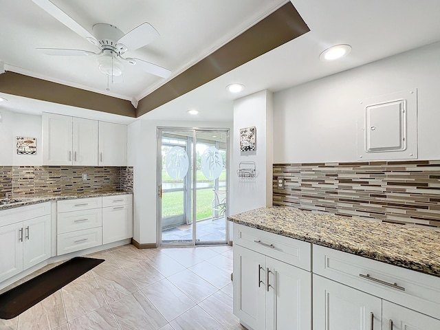 kitchen with backsplash, dark stone counters, white cabinets, crown molding, and ceiling fan