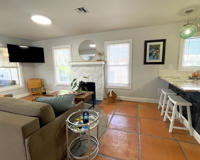 tiled living area featuring visible vents, a stone fireplace, and baseboards