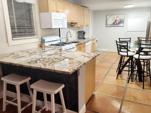 kitchen with a breakfast bar area, white appliances, a sink, decorative backsplash, and light brown cabinetry