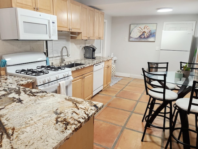 kitchen with white appliances, tasteful backsplash, light stone countertops, light brown cabinetry, and a sink