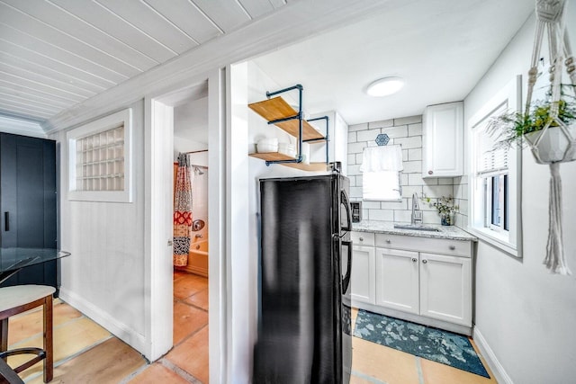 kitchen with a sink, white cabinetry, freestanding refrigerator, light stone countertops, and tasteful backsplash