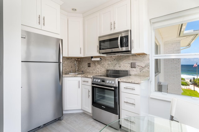 kitchen with backsplash, white cabinets, sink, stainless steel appliances, and a water view