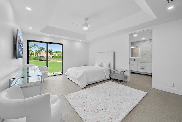 bedroom featuring a tray ceiling, ensuite bath, and ceiling fan