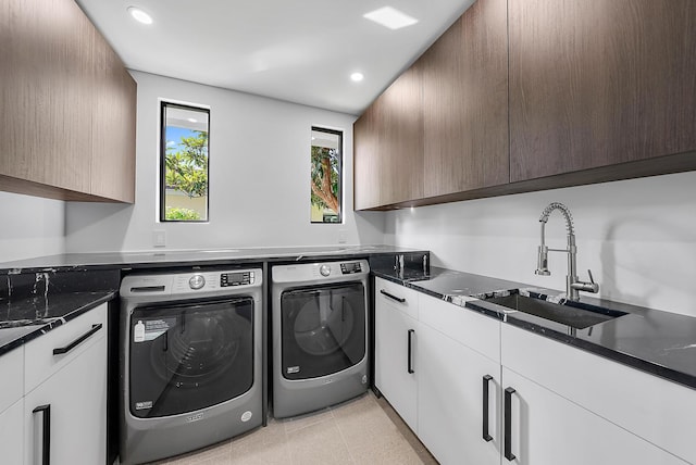 clothes washing area featuring washing machine and dryer, sink, light tile patterned floors, and cabinets