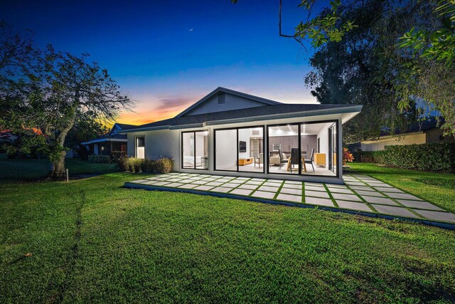 back house at dusk with a patio and a yard